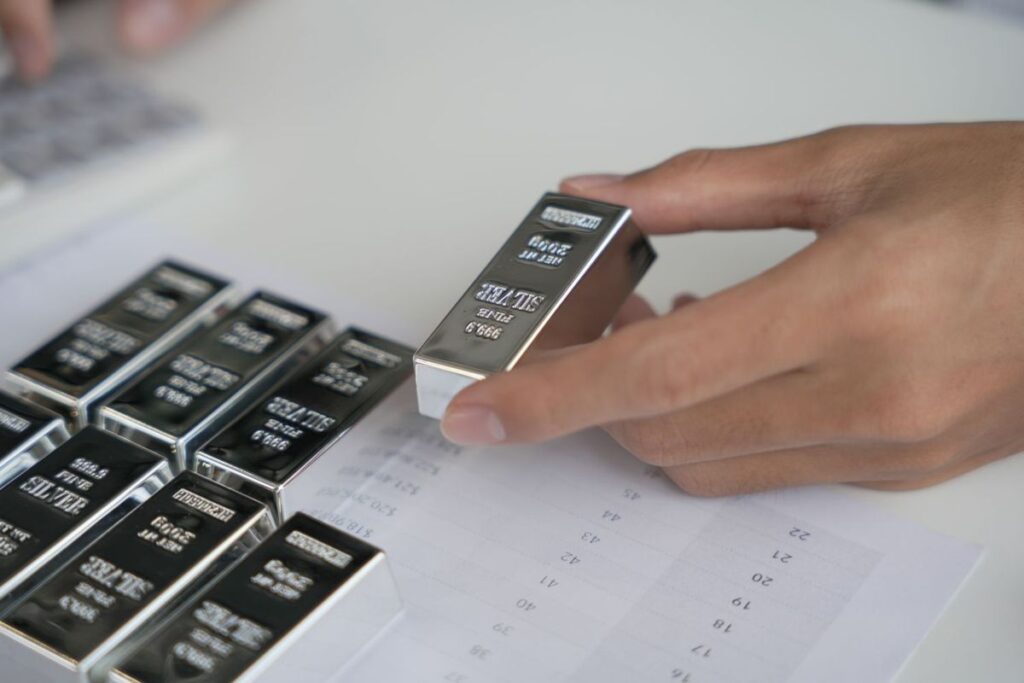 hand-holding-a-silver-bar-near-a-paper-sheet-with-price-charts-and-numbers-other-silver-bullion-bars-nearby.jpgid61659755width1200height800quality50coordinates02C02C02C0