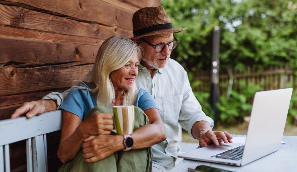 Elderly woman sitting beside her senior husband who is working on laptop.